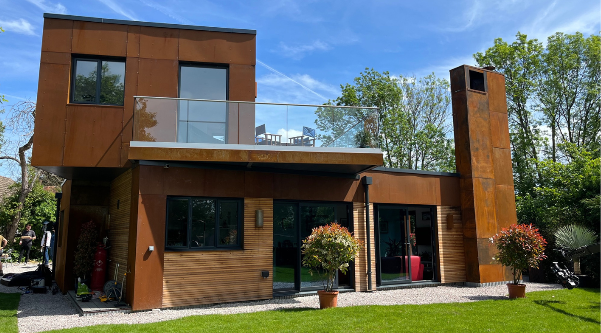 A rear view of the property showcasing the corten steel sheet and larch timber exterior combined with large french doors and glass balcony
