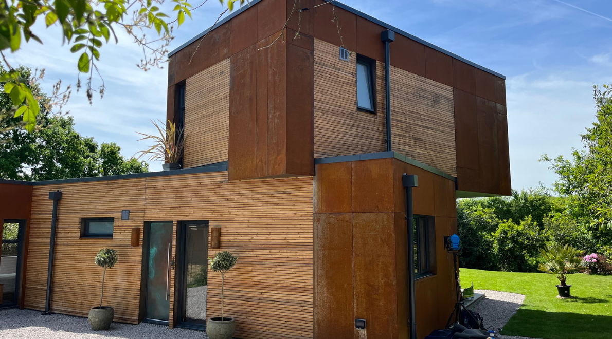 Wide shot showing the two levels of the modular build home surrounded by lush green grass and beautiful blue sky