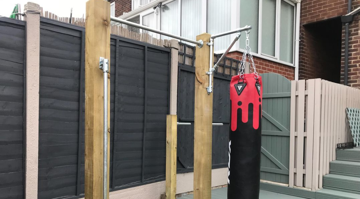 Home outdoor workout station built from wooden posts, galvanised tube and tube clamp fittings including a pull-up station, dips station and a punch bag for boxing
