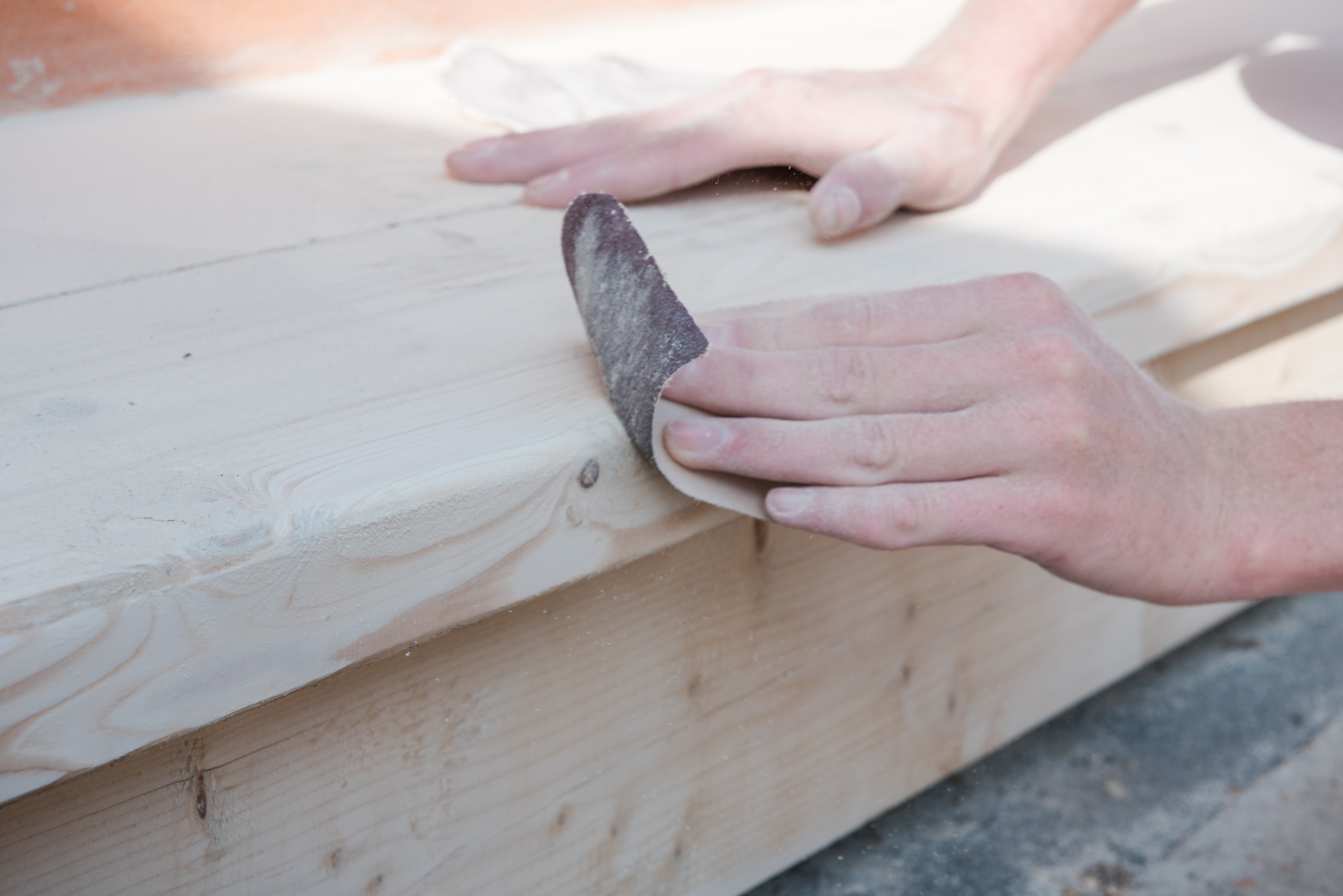 A mans hands polishing a timber scaffold board with sand paper giving the board a light, smooth finish