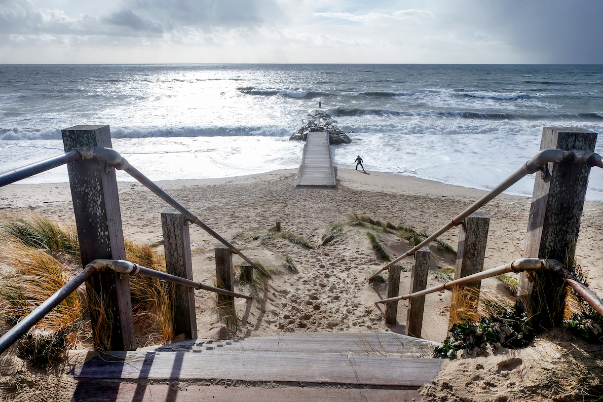 Weathered wooden steps leading down onto a sandy beach leading to the wide open sea with a wooden jetty leading to a small rock island, Southbourn, Christchurch, Dorset, England, UK