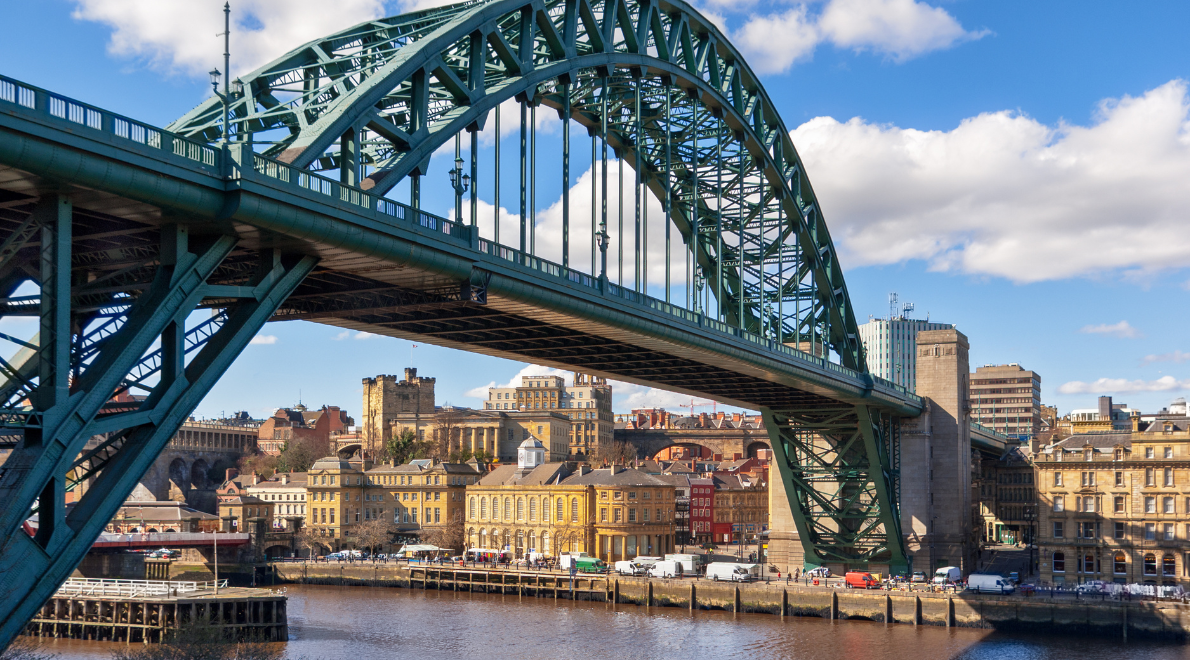 View from the water's edge beneath the Tyne Bridge - Majestic steel arches soar above, framing the sky and river with an intricate lattice of industrial beauty. The bridge's towering presence pays homage to a city's engineering prowess while harmonising with the natural flow of the water below