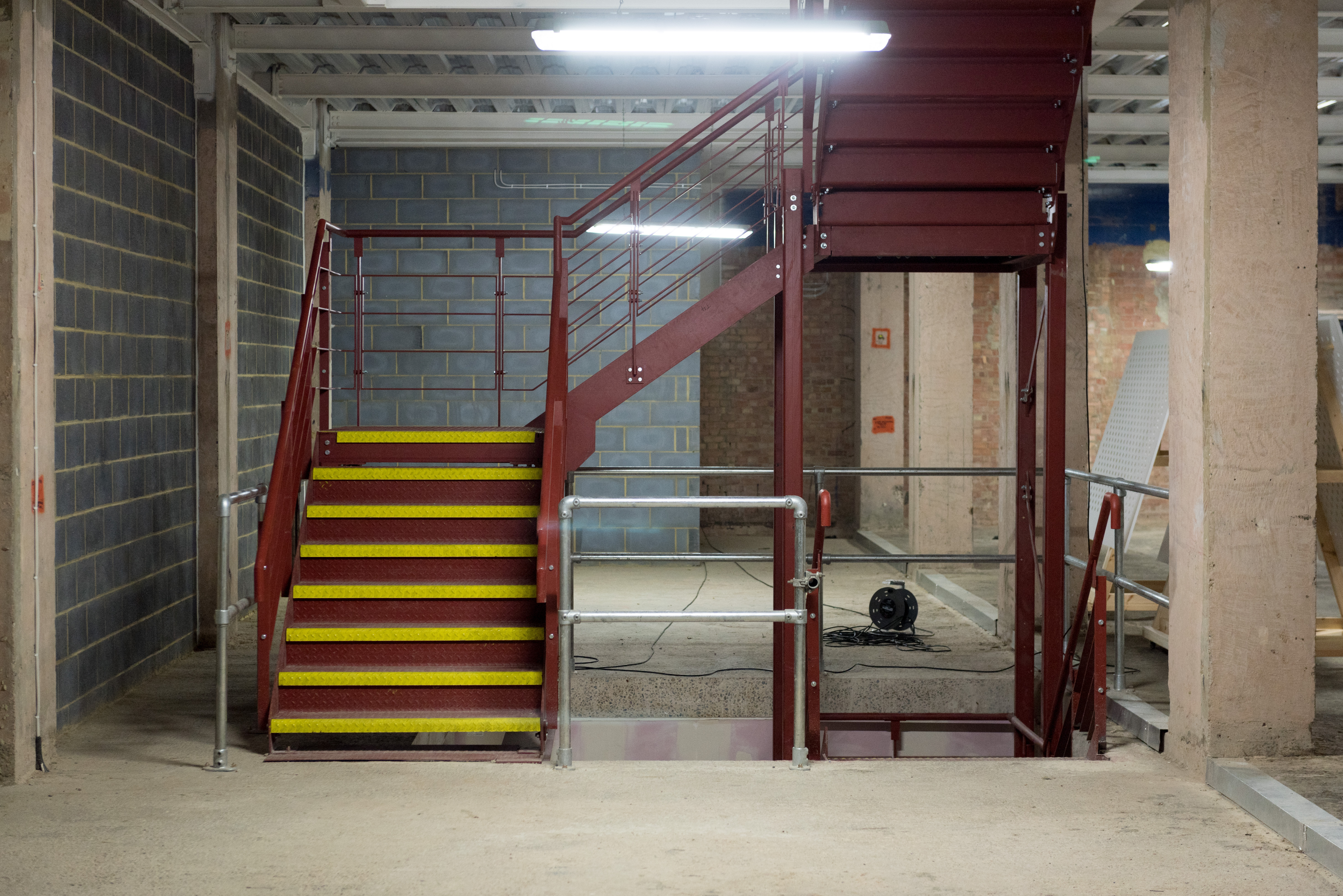 Steel staircase from the stock room up to the the main retail store with tube and clamp safety guardrails to protect staff members using this access point>
  </div>
  <div class=